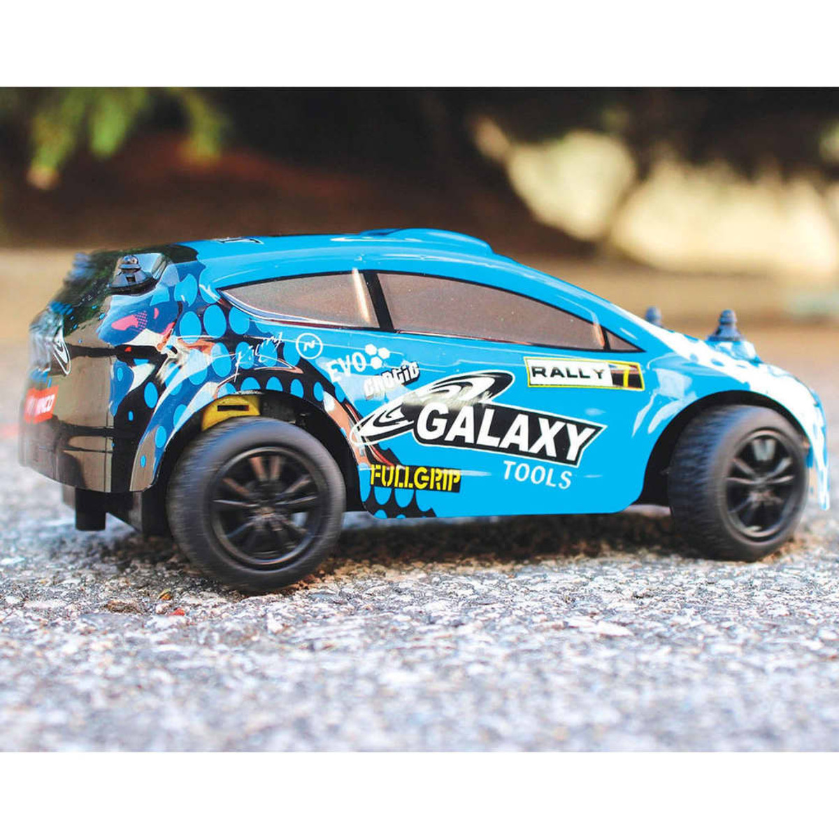 Un coche de juguete azul con techo blanco, ruedas negras y gráficos coloridos. Está sobre una superficie gris y tiene una pegatina.