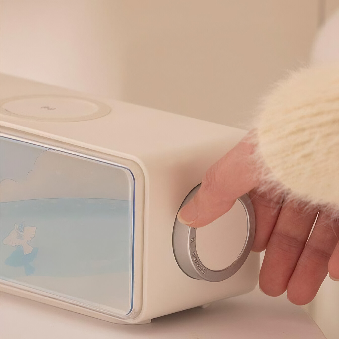 Eine Hand dreht am silbernen Einstellrad einer hellbeigen Klangmaschine mit Vogelgrafik.