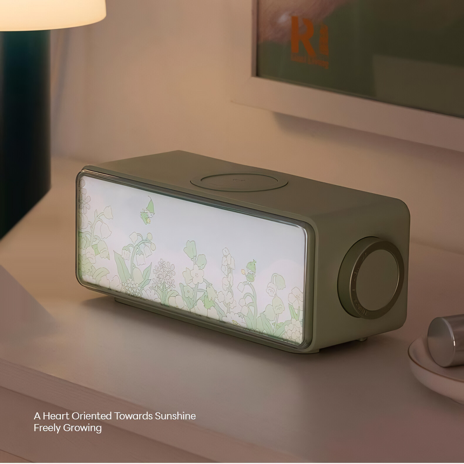 Ein grüner Lautsprecher auf einem Nachttisch mit floralem Bildschirm. Eine Lampe und andere Gegenstände befinden sich ebenfalls auf dem Tisch.