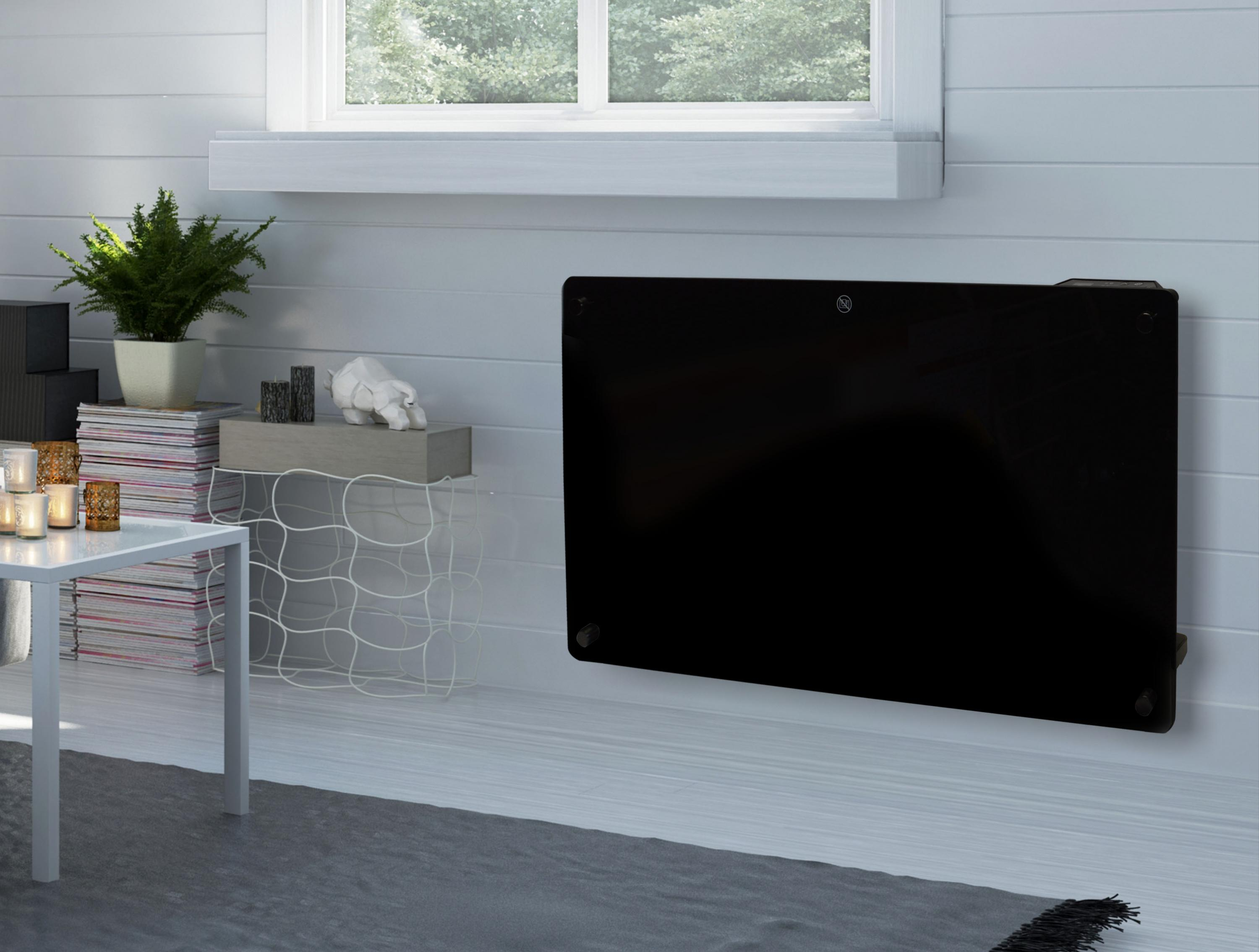 Un calefactor negro montado en la pared en una habitación con una ventana y una mesa blanca con velas y decoración.