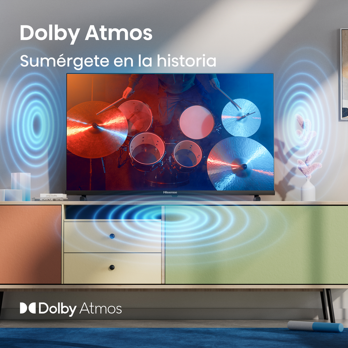 Telewizor pokazujący perkusistę na scenie z tekstem: Dolby Atmos. Telewizor stoi na szafce z niebieskimi falami.