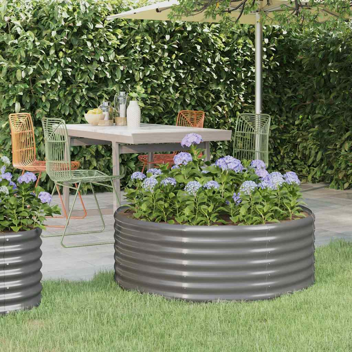 Gartenszene mit großem, dunkelgrauen, runden Wellblech-Pflanzgefäß mit blauen Blüten.
