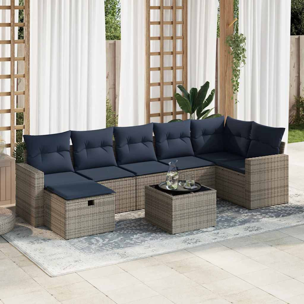 Terrassen-Set mit grauem Korbgeflecht, blauen Kissen und einem Couchtisch mit Glasplatte.