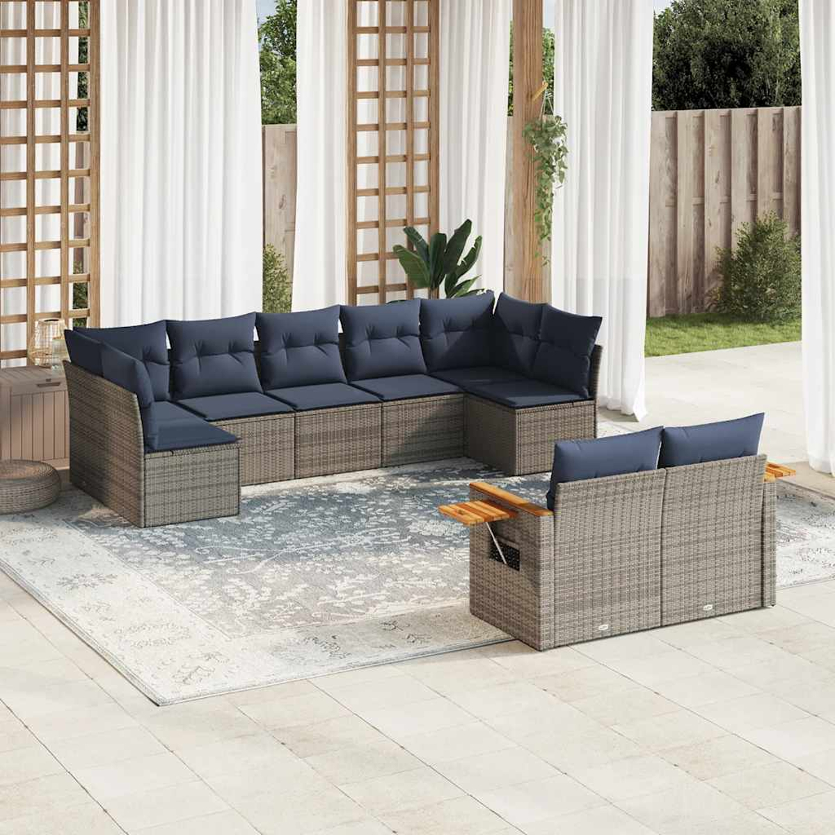 Un sofá seccional de ratán gris con cojines azules, colocado en un patio con cortinas blancas y una alfombra.