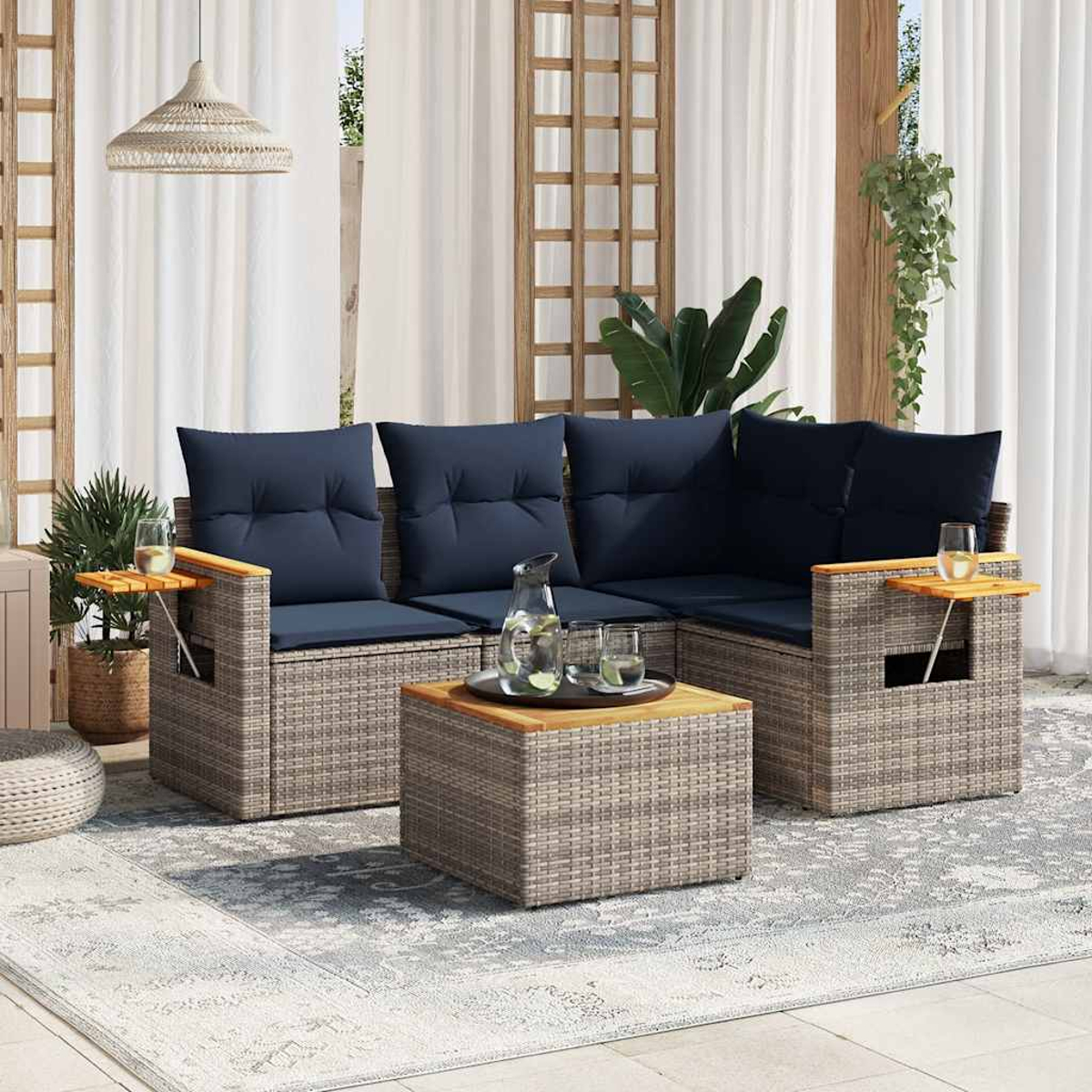 Terrassenset mit grauen Korbwarenmöbeln, blauen Kissen und hölzernen Beistelltischen auf einem gemusterten Teppich.