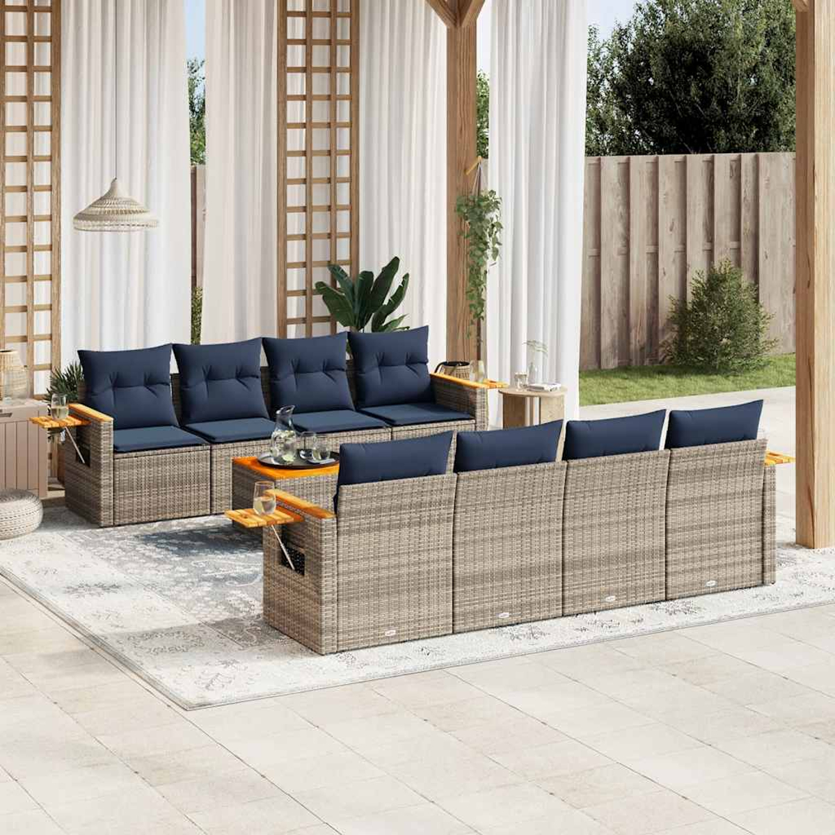Ein Outdoor-Sofagarnitur mit blauen Kissen, Beistelltischen und einem Teppich. Weiße Vorhänge und eine Holzkonstruktion im Hintergrund.