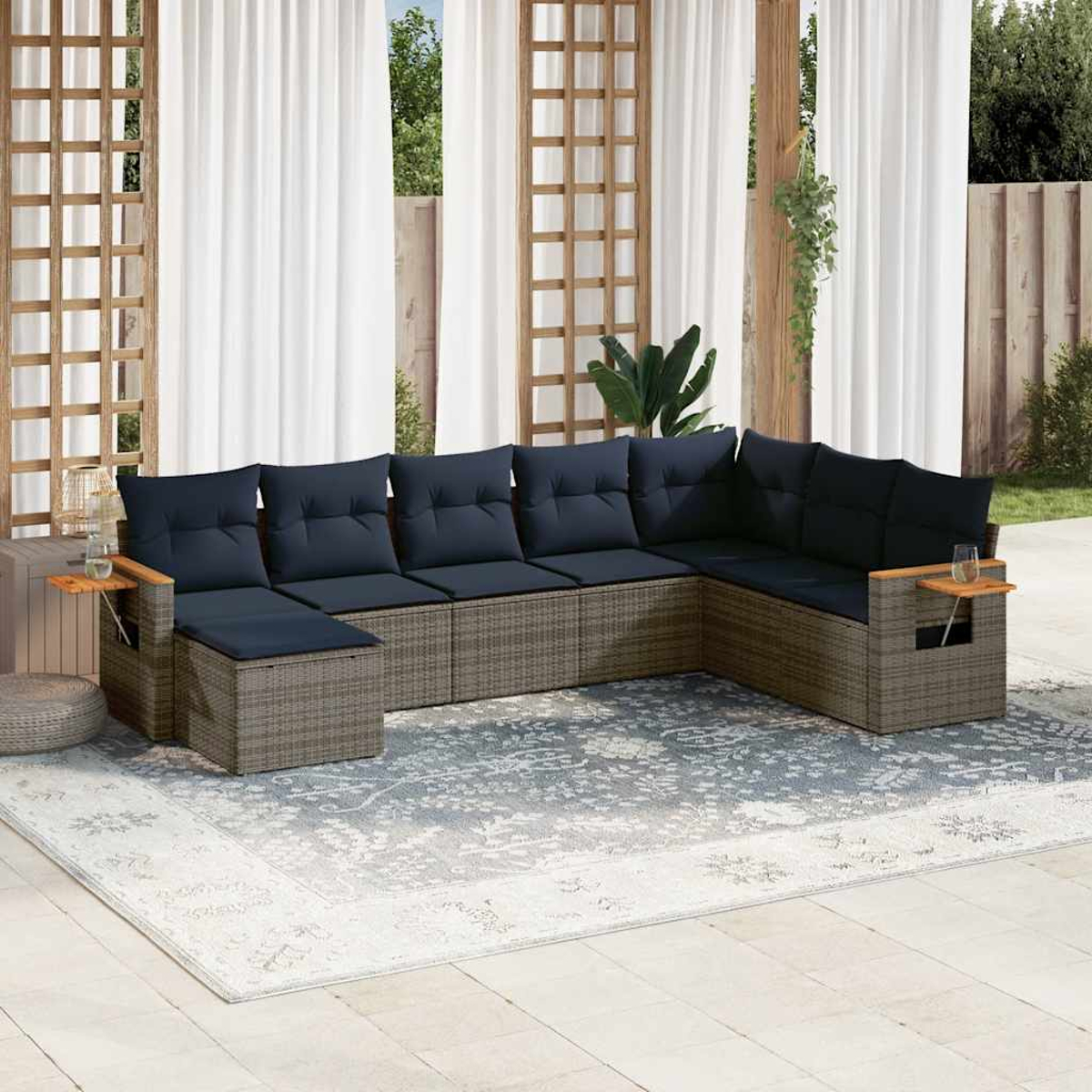 Ein Ecksofa für den Außenbereich mit grauem Korbgeflecht, marineblauen Kissen, hölzernen Beistelltischen und einem gemusterten Teppich.