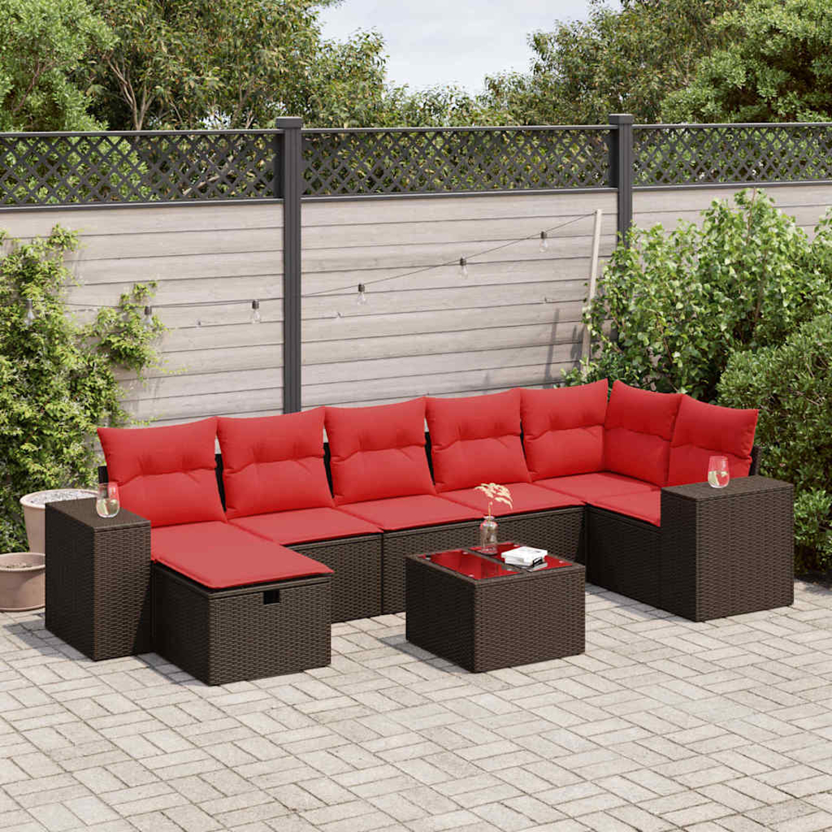 Eine Terrasse mit einem dunkelbraunen Ecksofa, roten Kissen und einem Couchtisch mit Glasplatte.