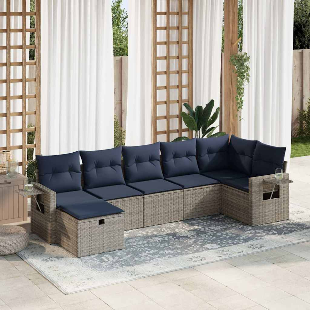 Ein graues Rattan-Ecksofa mit marineblauen Kissen steht auf einem gemusterten Teppich. Weiße Vorhänge im Hintergrund.