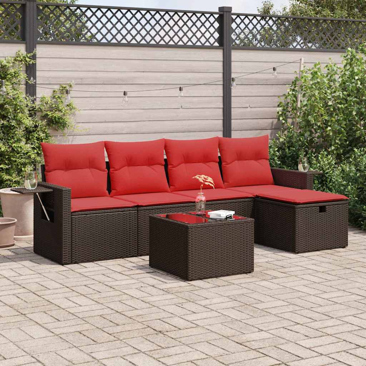 Gartenmöbel mit roten Kissen und einem kleinen Tisch. Hintergrund: Zaun und Grün.