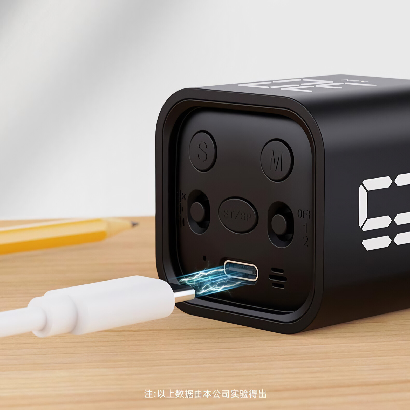 Ein schwarzer Würfel-Timer mit einem weißen Ladekabel. Der Hintergrund ist ein Holztisch.