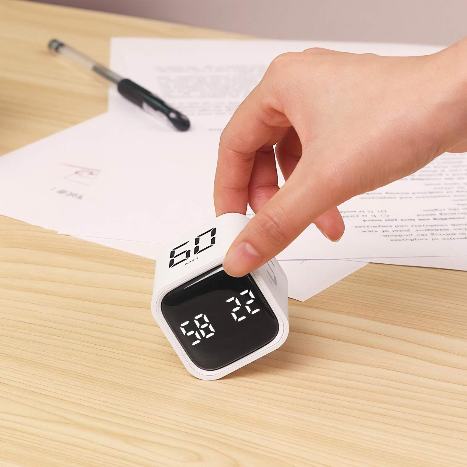 Ein würfelförmiger Timer mit digitaler Anzeige wird von einer Hand auf einem Holztisch gehalten.