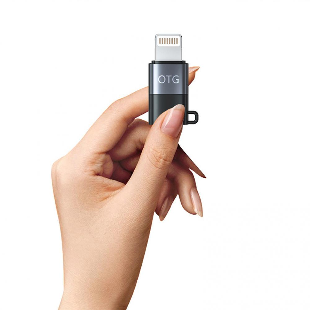 Eine Hand, die einen kleinen schwarzen und silbernen Adapter mit den Buchstaben OTG darauf hält.