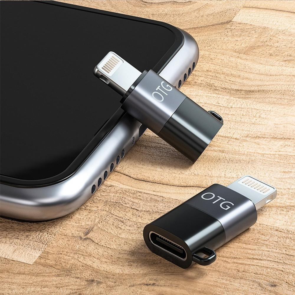 Zwei kleine schwarze und silberne Adapter, die auf einer Holzoberfläche neben einem Smartphone liegen.
