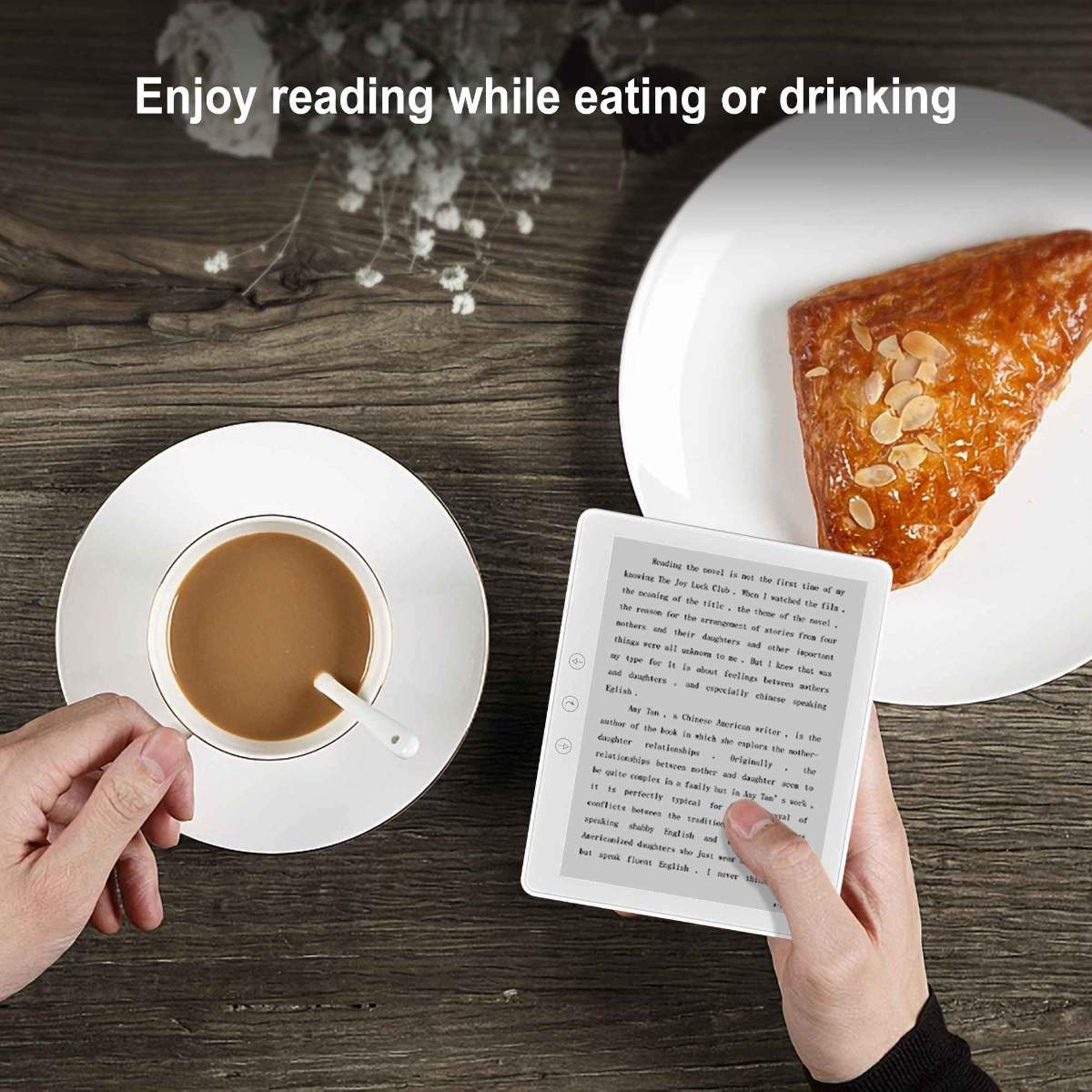 Hand hält weißen E-Reader, Kaffee und Gebäck auf Holztisch.