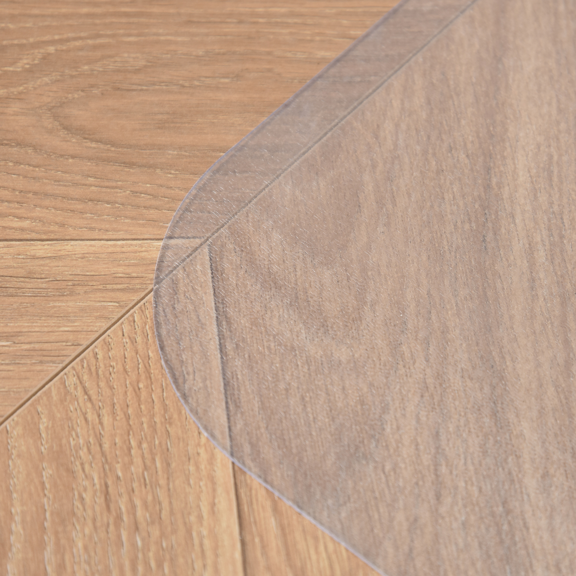 Un tappetino di plastica trasparente su un pavimento in legno. Il tappetino ha angoli arrotondati e protegge la superficie.