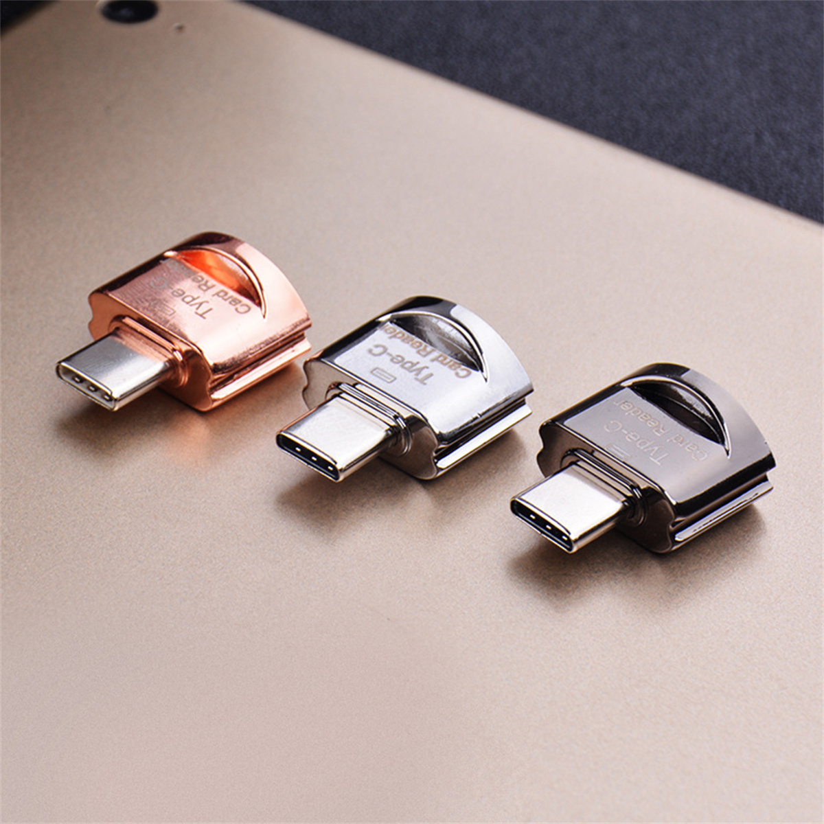 Drei Typ-C-Kartenleser in Roségold, Silber und Schwarz auf einer goldenen Oberfläche platziert.
