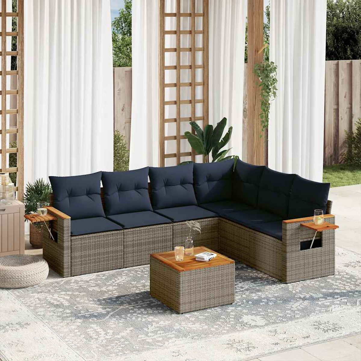 Rattan-Outdoor-Sofagarnitur mit blauen Kissen, Couchtisch und Beistelltischen mit Getränken. Weiße Vorhänge.