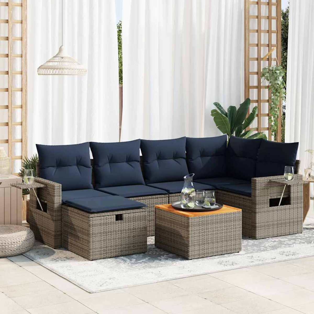 Outdoor-Rattan-Sofagarnitur mit blauen Kissen, Couchtisch und Beistelltischen mit Gläsern. Weiße Vorhänge.