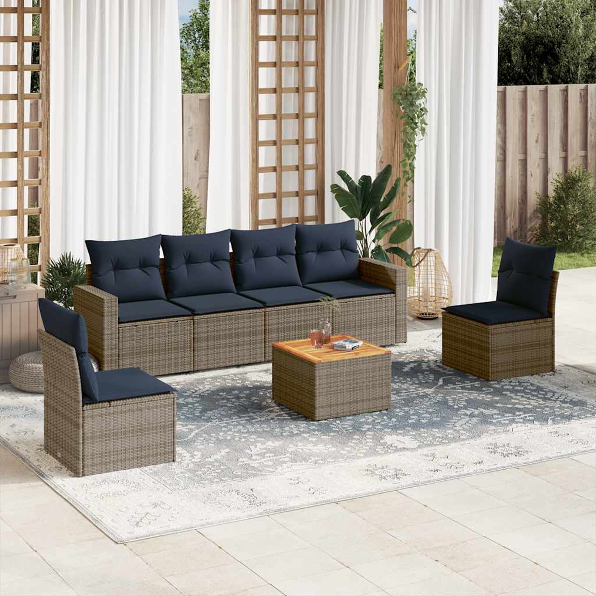 Eine Terrasse mit grauen Korbmöbeln, blauen Kissen, einem Teppich und weißen Vorhängen.