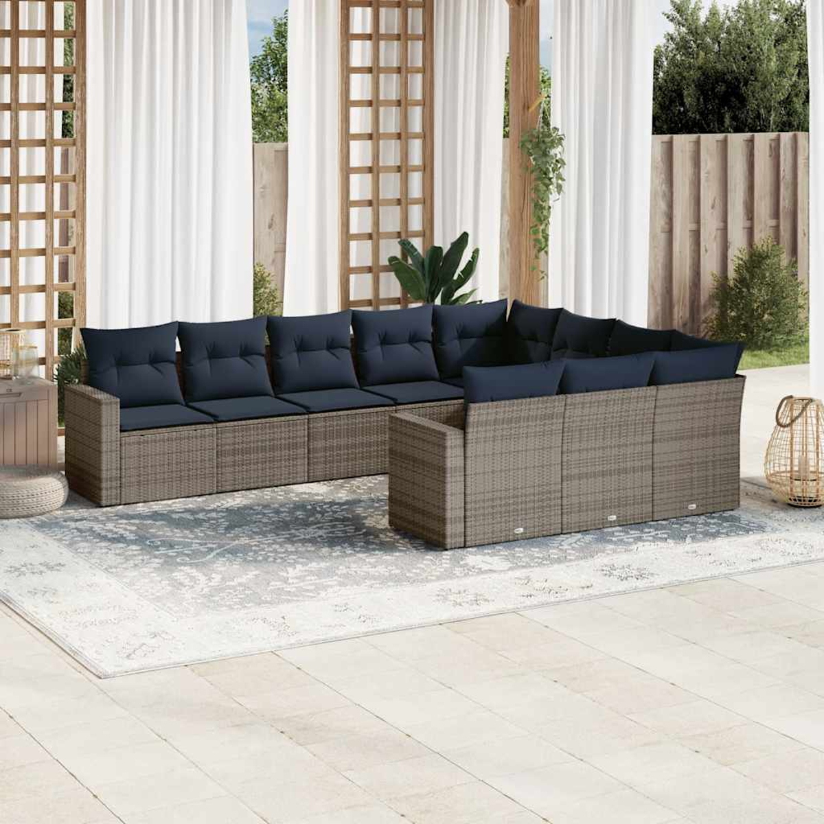 Garten-Rattanmöbel-Set mit marineblauen Kissen, Tisch und Teppich, in einem Garten mit weißen Vorhängen.