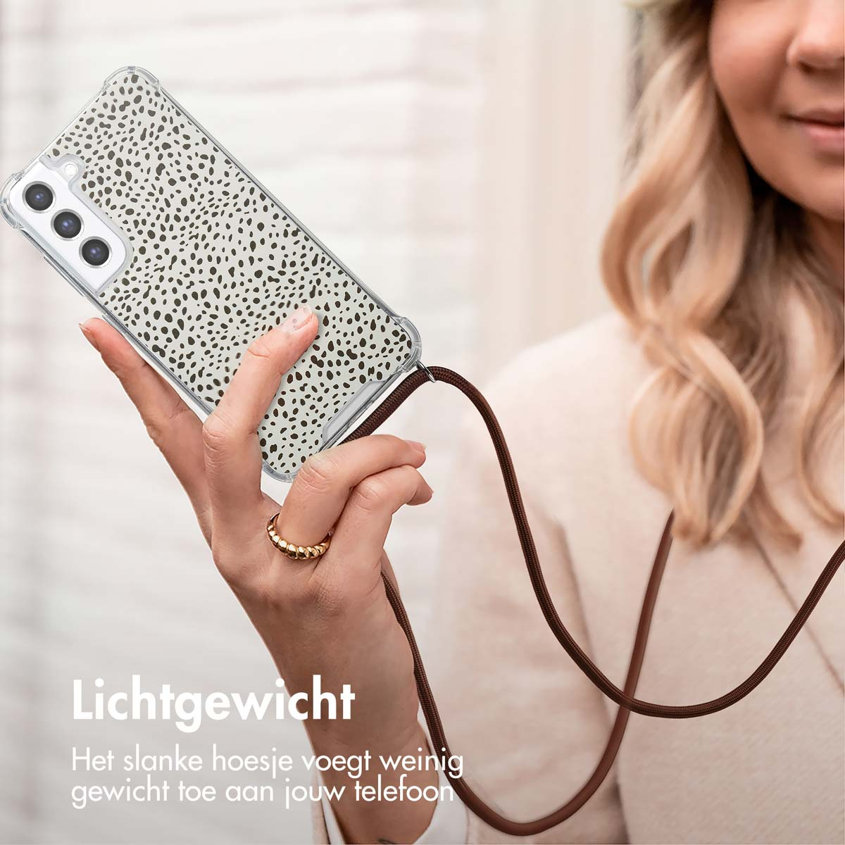 Vrouw houdt telefoon vast met een hoesje met patroon en een bruine band. Ring aan vinger.
