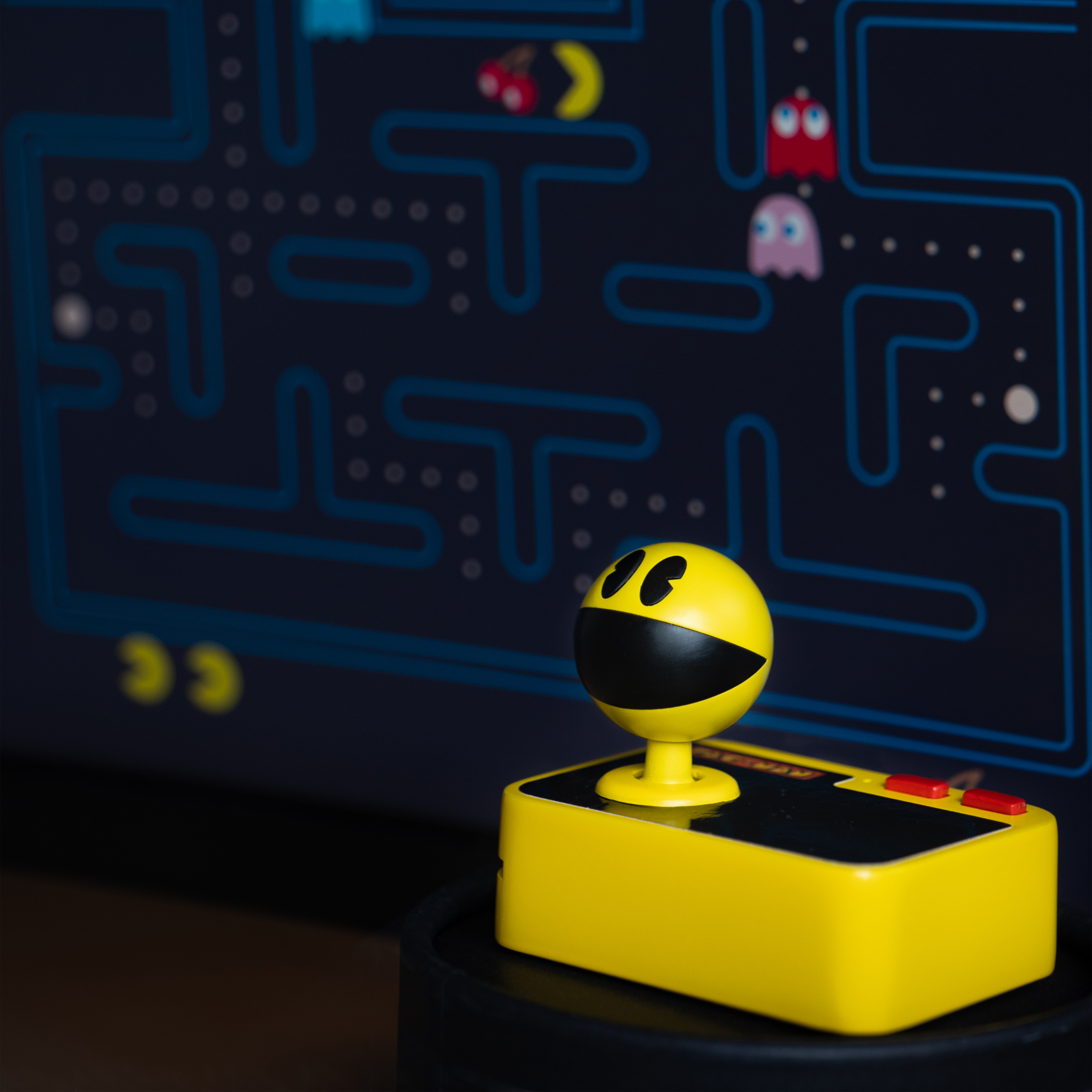Gele Pac-Man-controller met een zwart gezicht en joystick, voor een Pac-Man-spelscherm.
