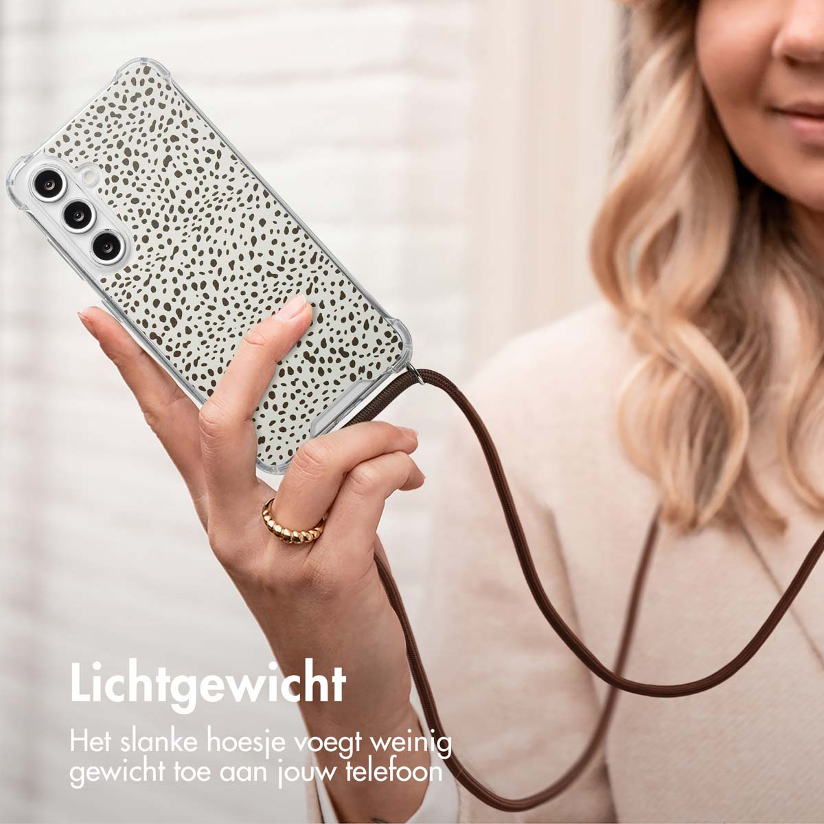 La main d'une femme tenant un téléphone avec une coque transparente à taches marron et une sangle marron.