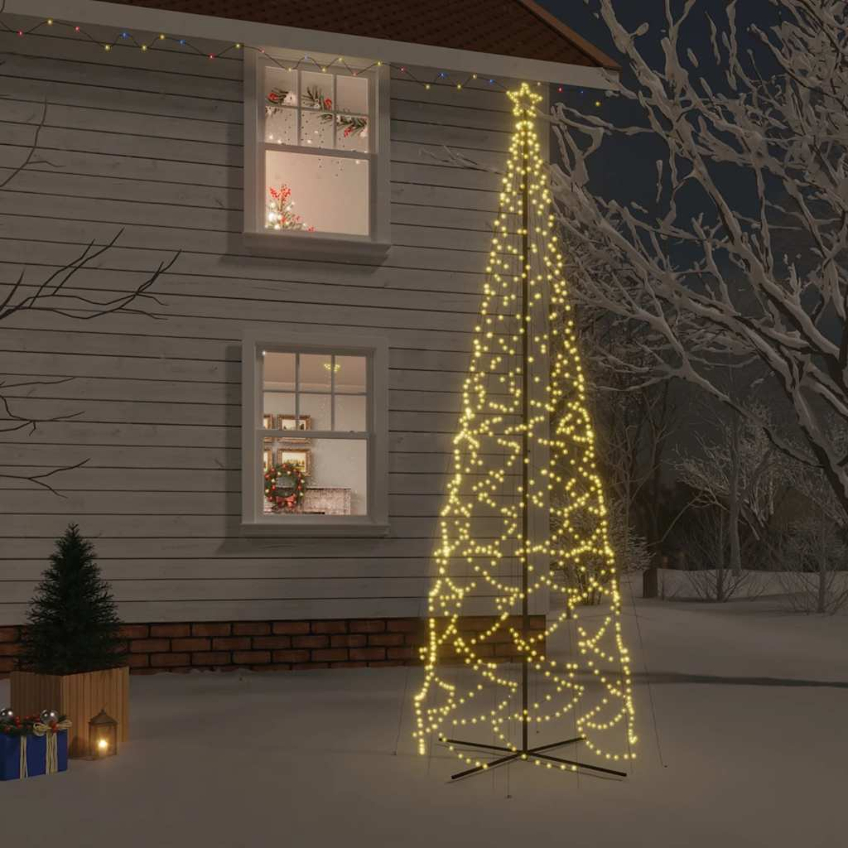 Ein beleuchteter Weihnachtsbaum vor einem Haus bei Nacht. Schnee am Boden.