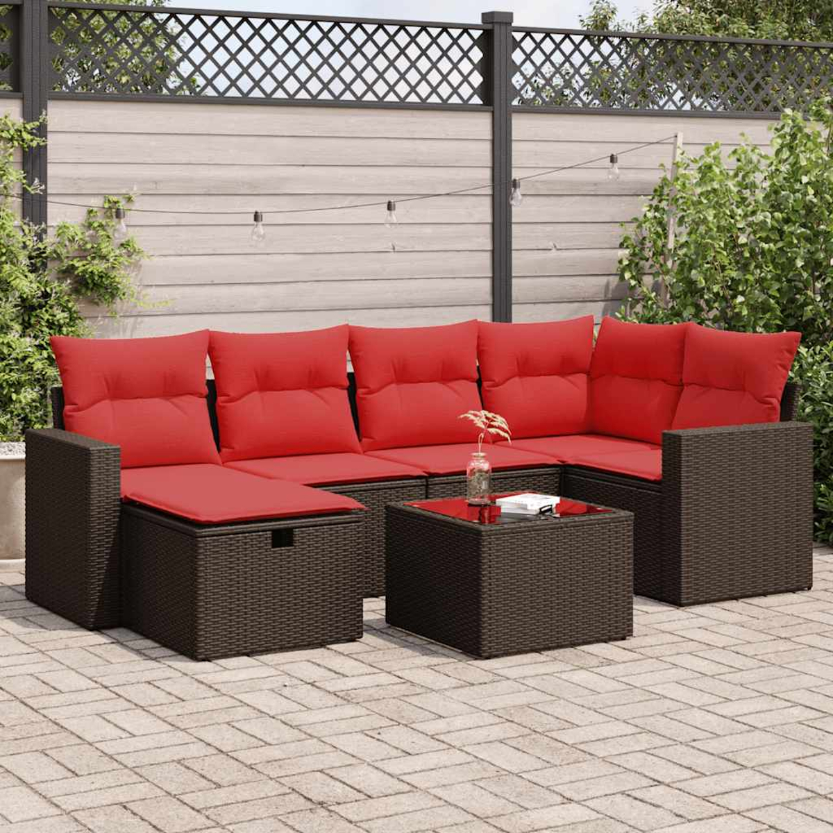 Geflochtenes Outdoor-Ecksofa mit roten Kissen und Couchtisch auf einer Backstein-Terrasse.