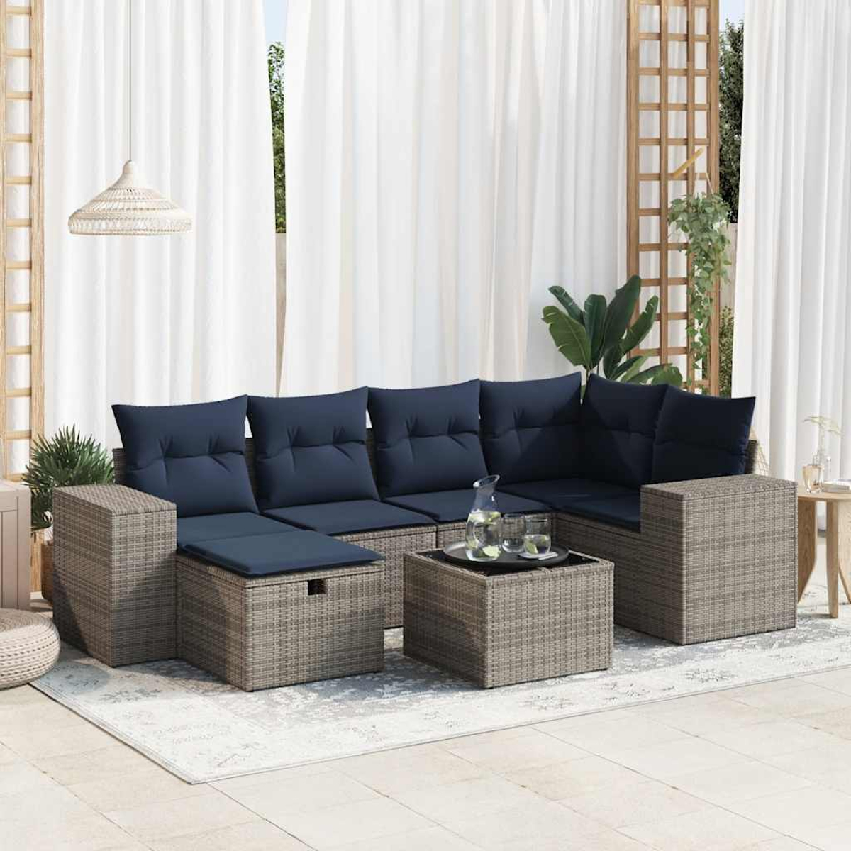 Rattansofa-Set mit marineblauen Kissen, Glastisch, Teppich und weißen Vorhängen im Freien.