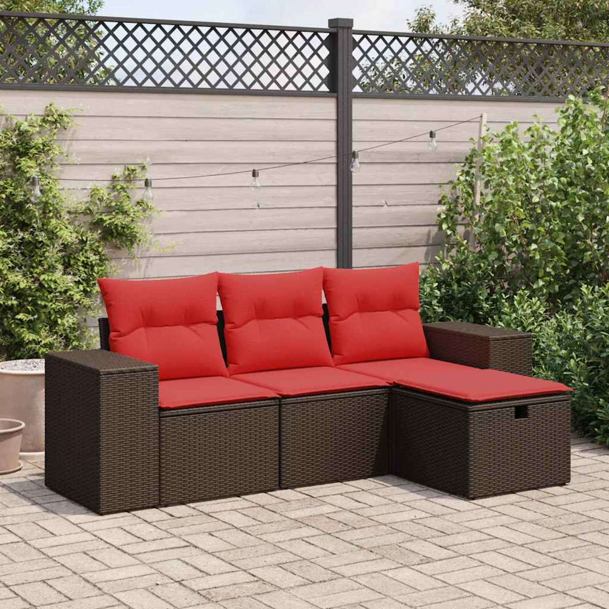 Braunes Rattansofa-Set mit roten Kissen auf einer Ziegelterrasse. Grün und Zaun im Hintergrund.