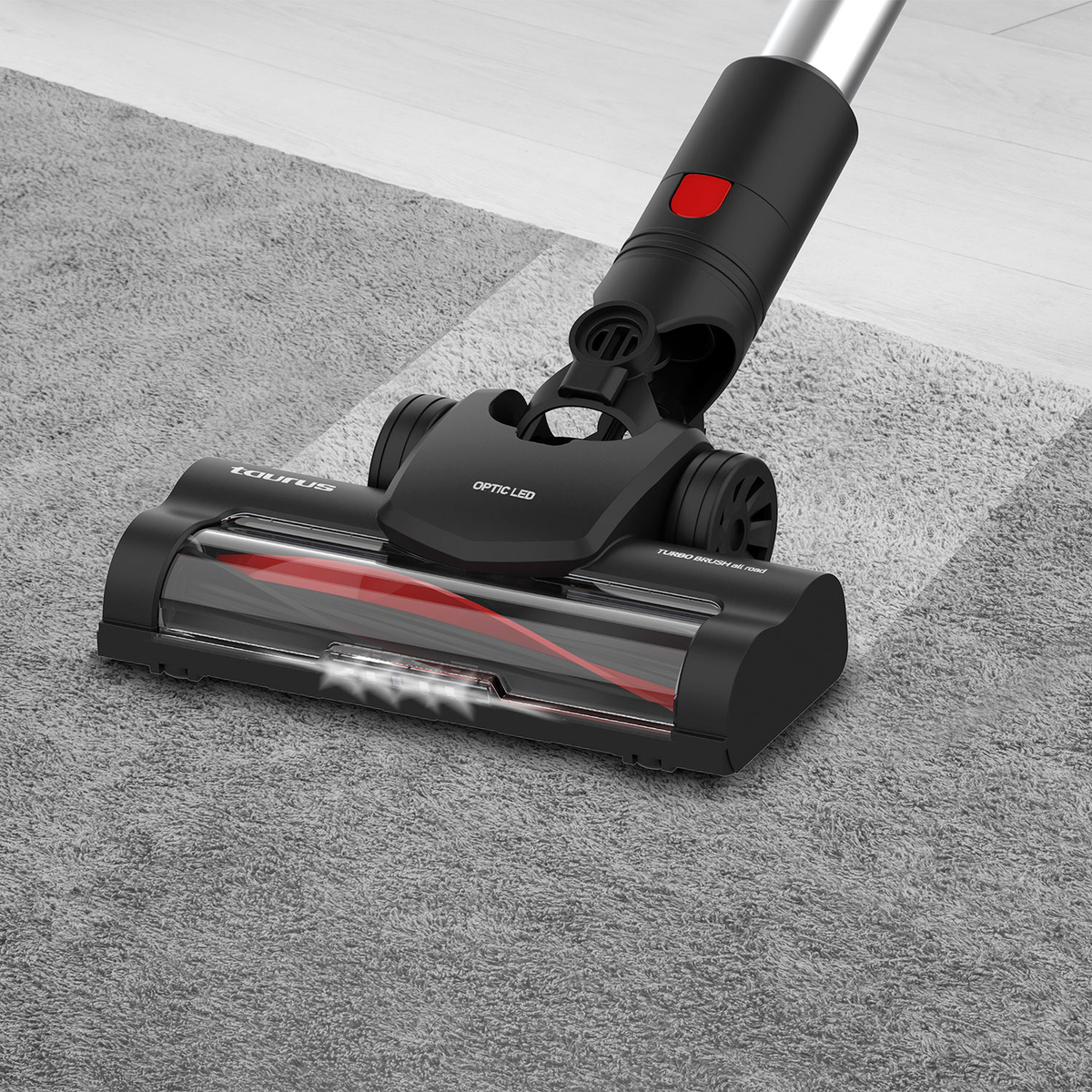 Un cabezal de aspiradora negro y rojo limpiando una alfombra gris, con la marca Taurus visible.