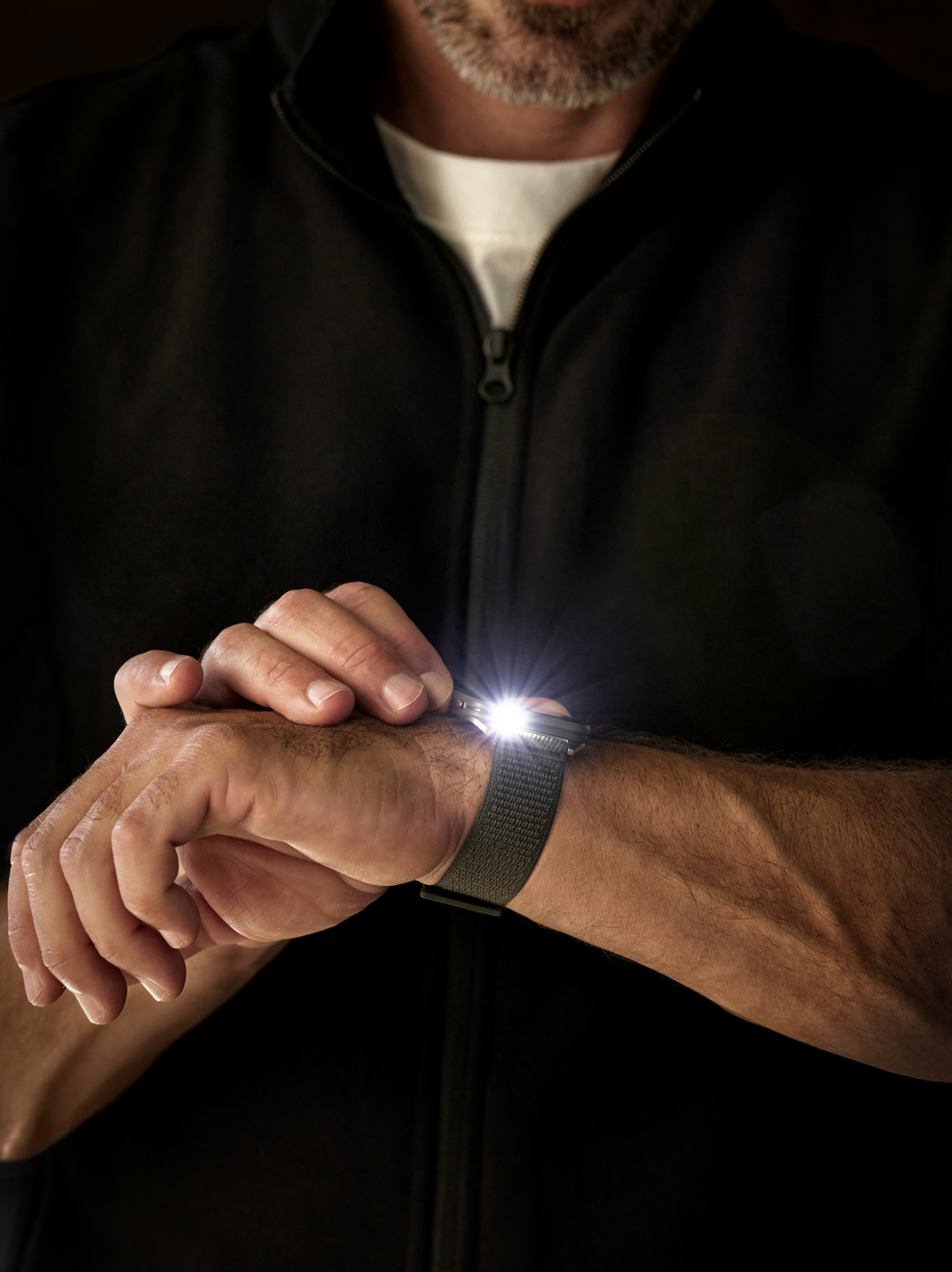 Ein Mann mit einer Uhr am Handgelenk. Der Bildschirm der Uhr leuchtet und scheint auf den Betrachter zu.