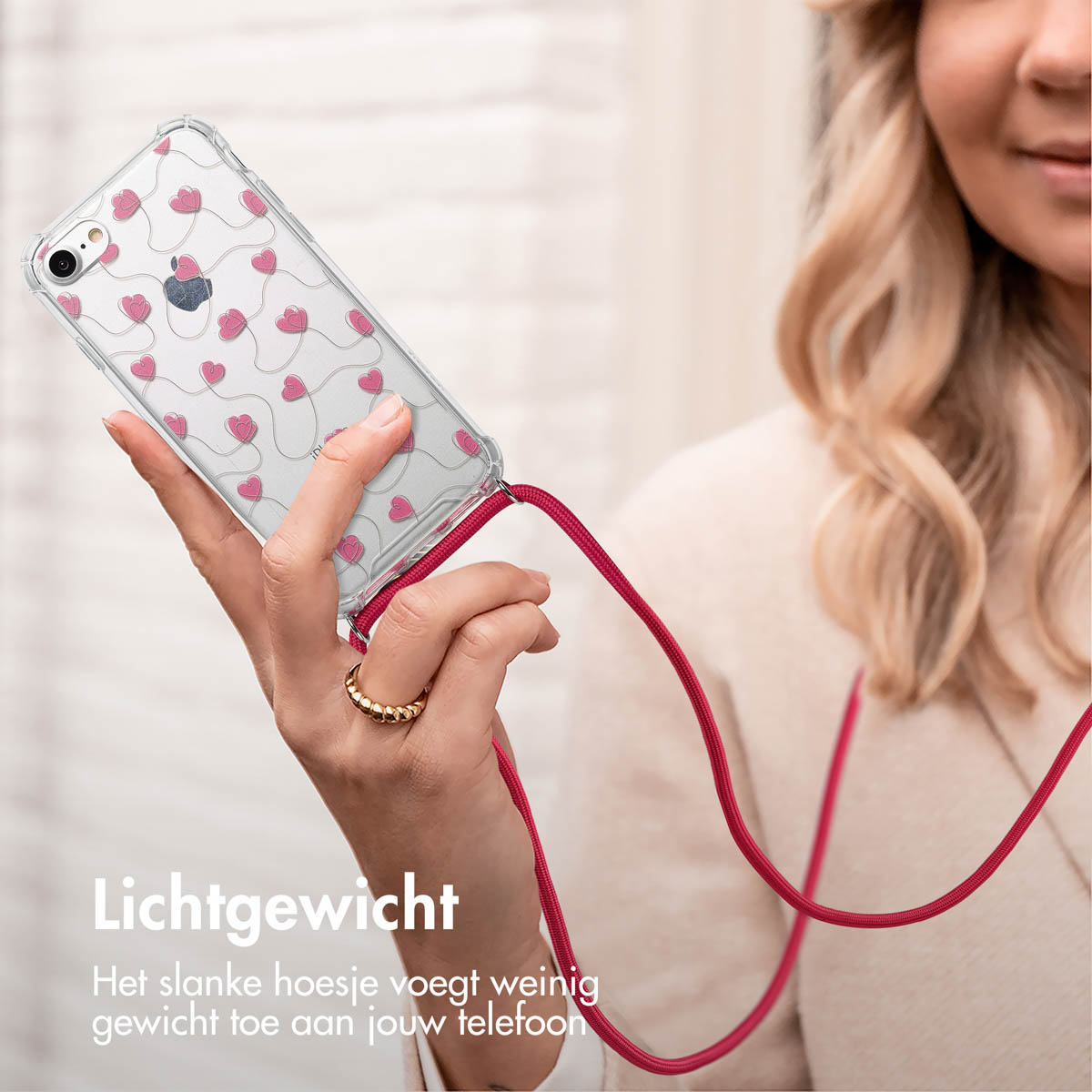 Een vrouw die een telefoon vasthoudt met een doorzichtig hoesje en roze hartjes, met een rood koord.