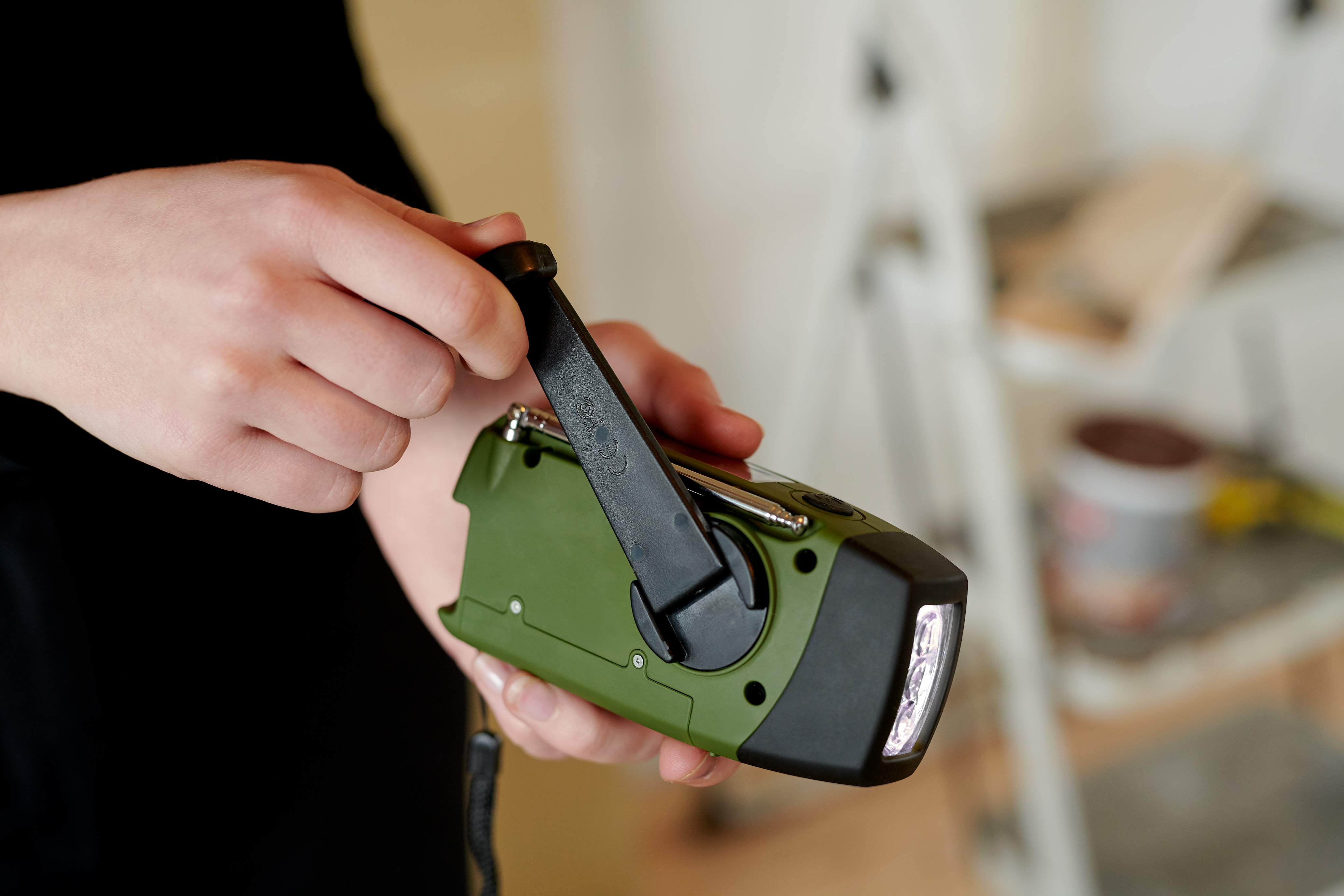 Ręce kręcą korbą zielonego radia. Światło świeci z radia.