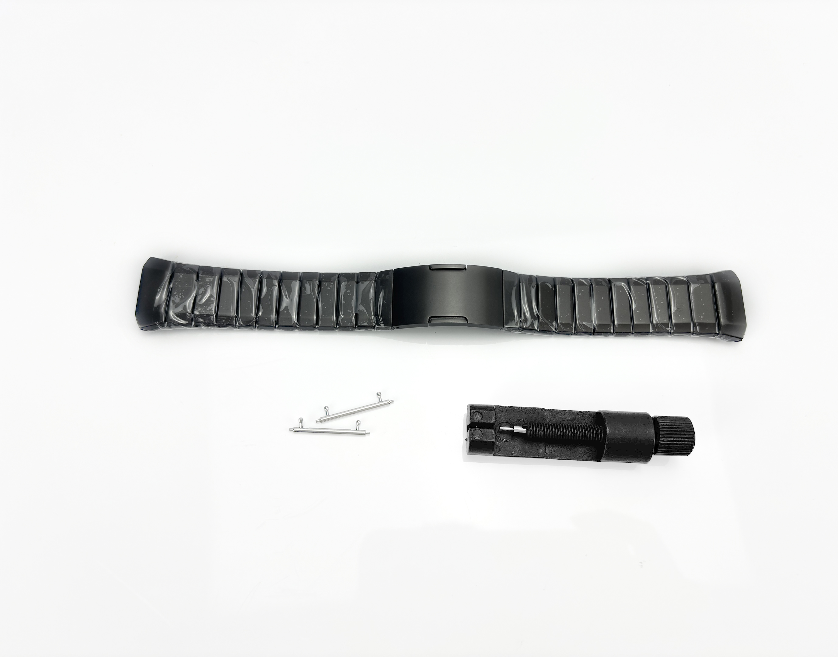 Ein schwarzes Uhrenarmband mit Werkzeugen zur Größenanpassung. Auf weißer Oberfläche. Die Werkzeuge sind silber und schwarz.