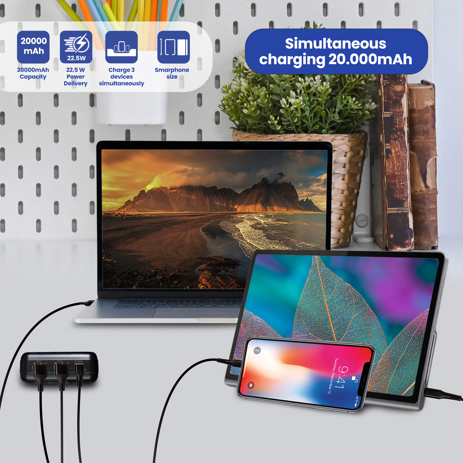 Dispositivos cargándose en un escritorio con un portátil, tableta, teléfono, batería externa y cables sobre fondo claro.