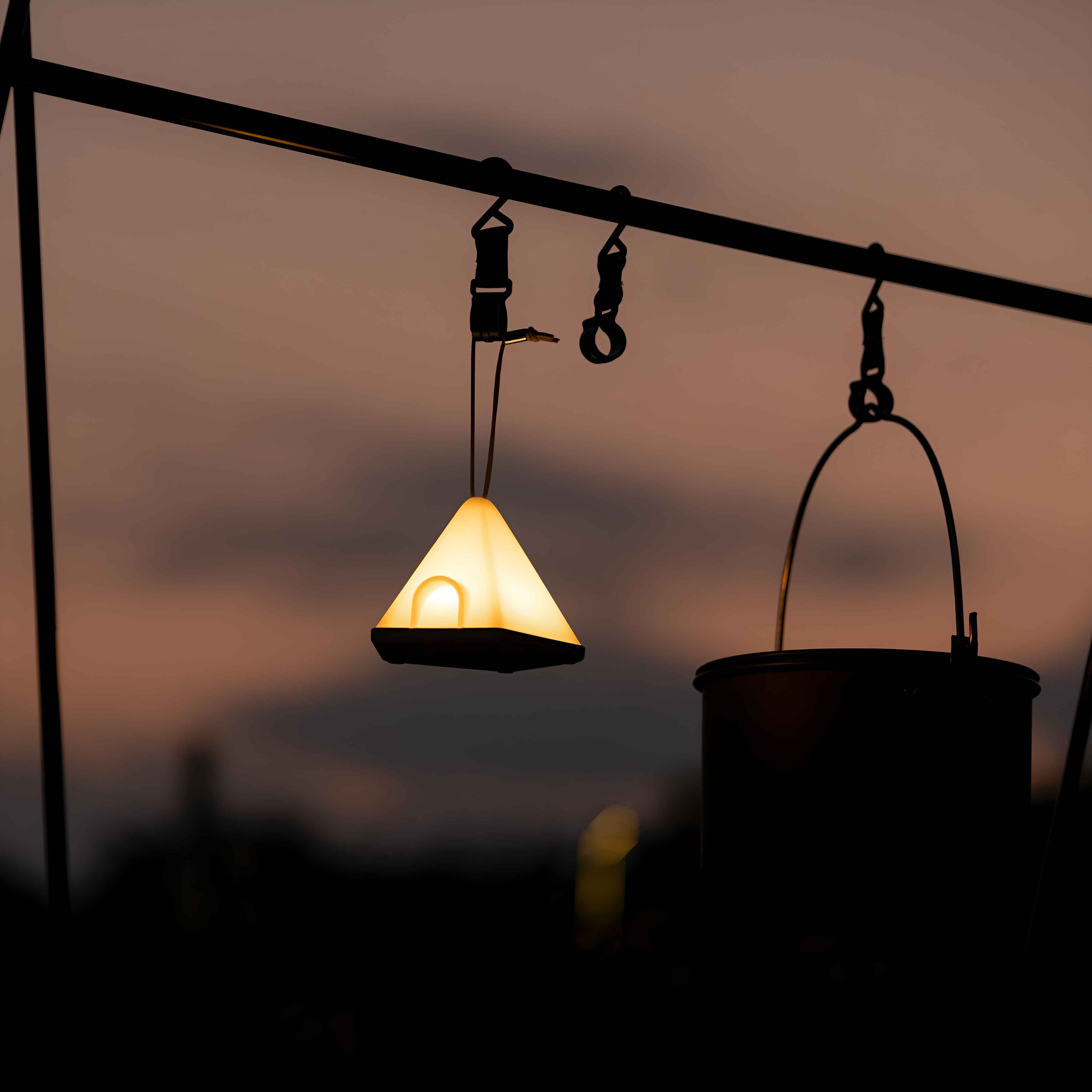 Eine leuchtende, weiße, dreieckige Lampe hängt an einer dunklen Metallstruktur vor Sonnenuntergang.