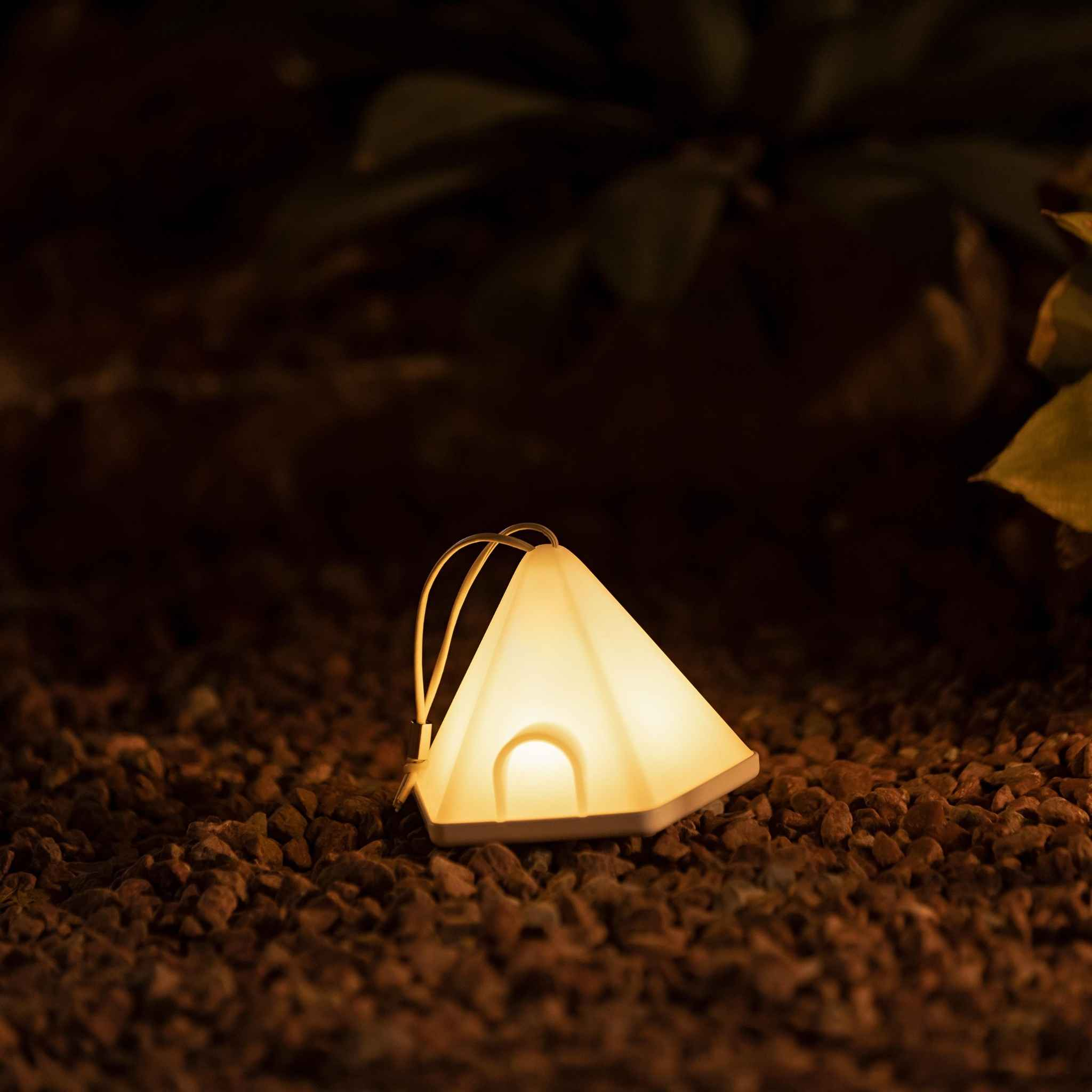 Eine weiße, dreieckige Lampe liegt auf dem Boden inmitten kleiner Steine mit dunklem Hintergrund.