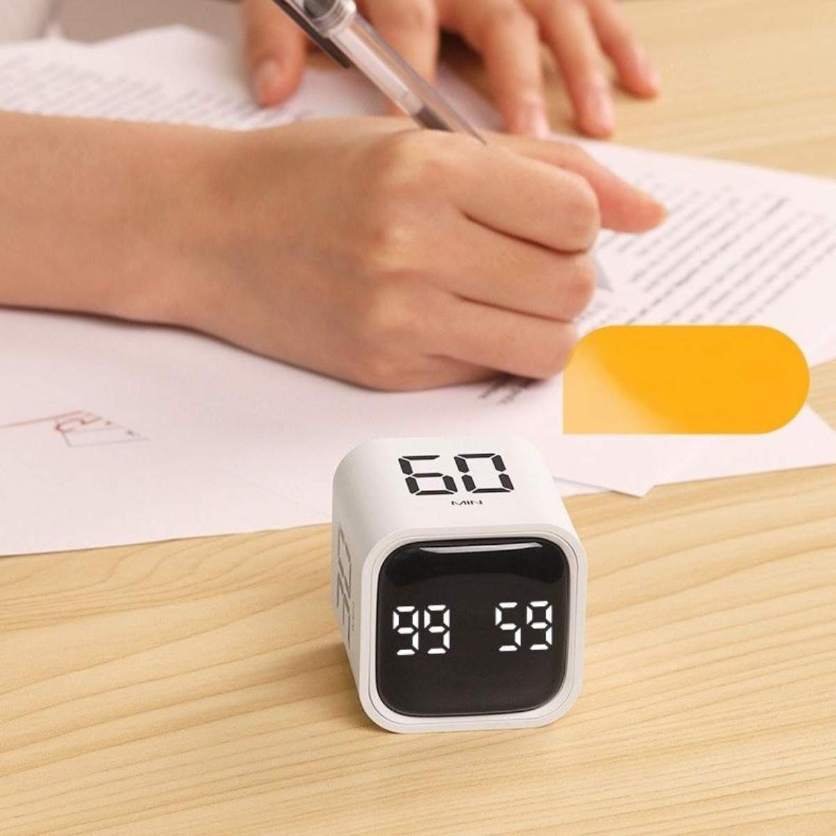 Ein weißer Würfel-Timer zeigt '60' und zählt von '99 59' herunter. Eine Hand schreibt.