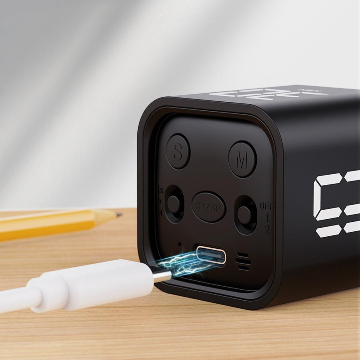 Schwarzer, würfelförmiger digitaler Wecker mit weißem Ladekabel.