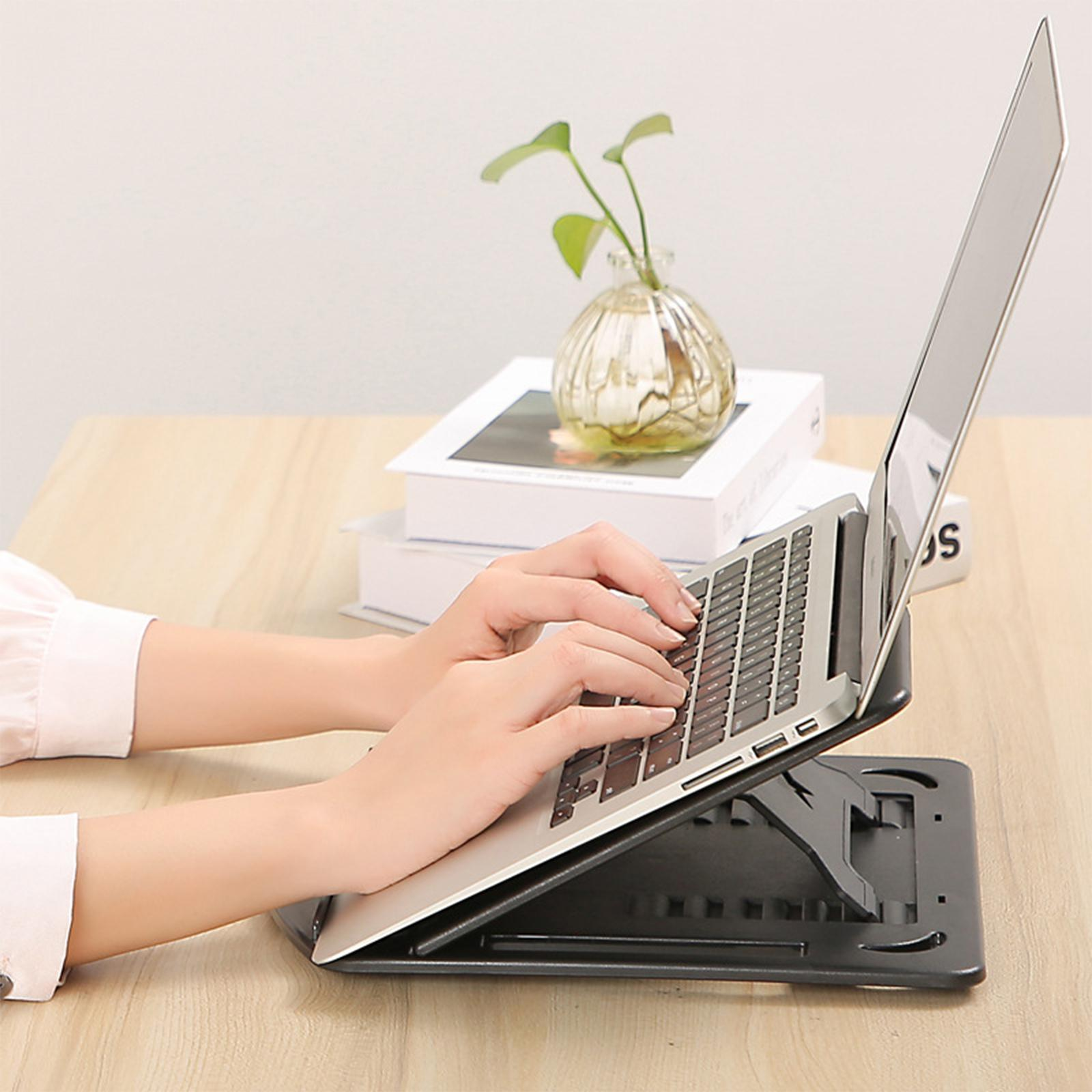 Eine Person tippt auf einem Laptop auf einem Ständer. Eine Vase mit Blumen und Bücher stehen auf dem Schreibtisch.