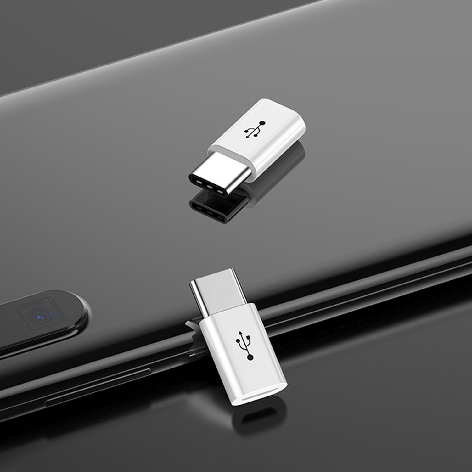 Zwei weiße USB-C-Adapter liegen auf einer reflektierenden schwarzen Oberfläche. Einer ist fokussiert, der andere unscharf.