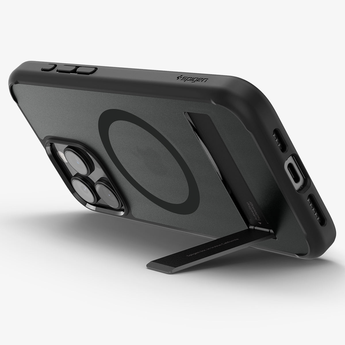 Coque de téléphone noire avec support et anneau MagSafe sur surface blanche, en angle et de profil.