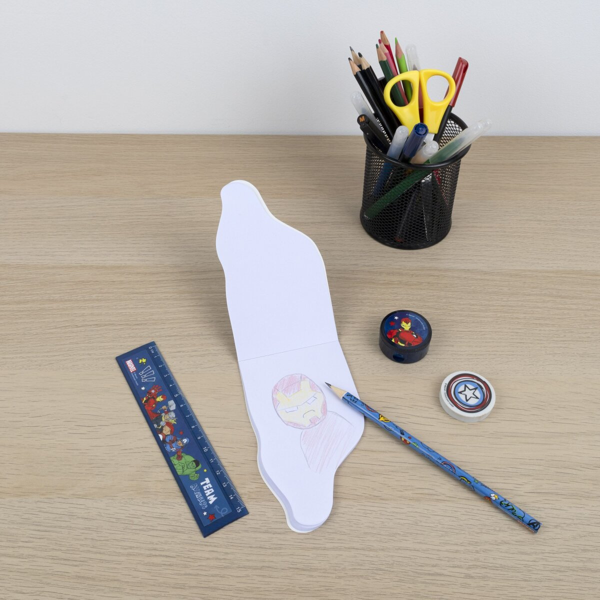 Desk with stationery: pencils, scissors, ruler, eraser, sharpener, and a drawing of Iron Man.