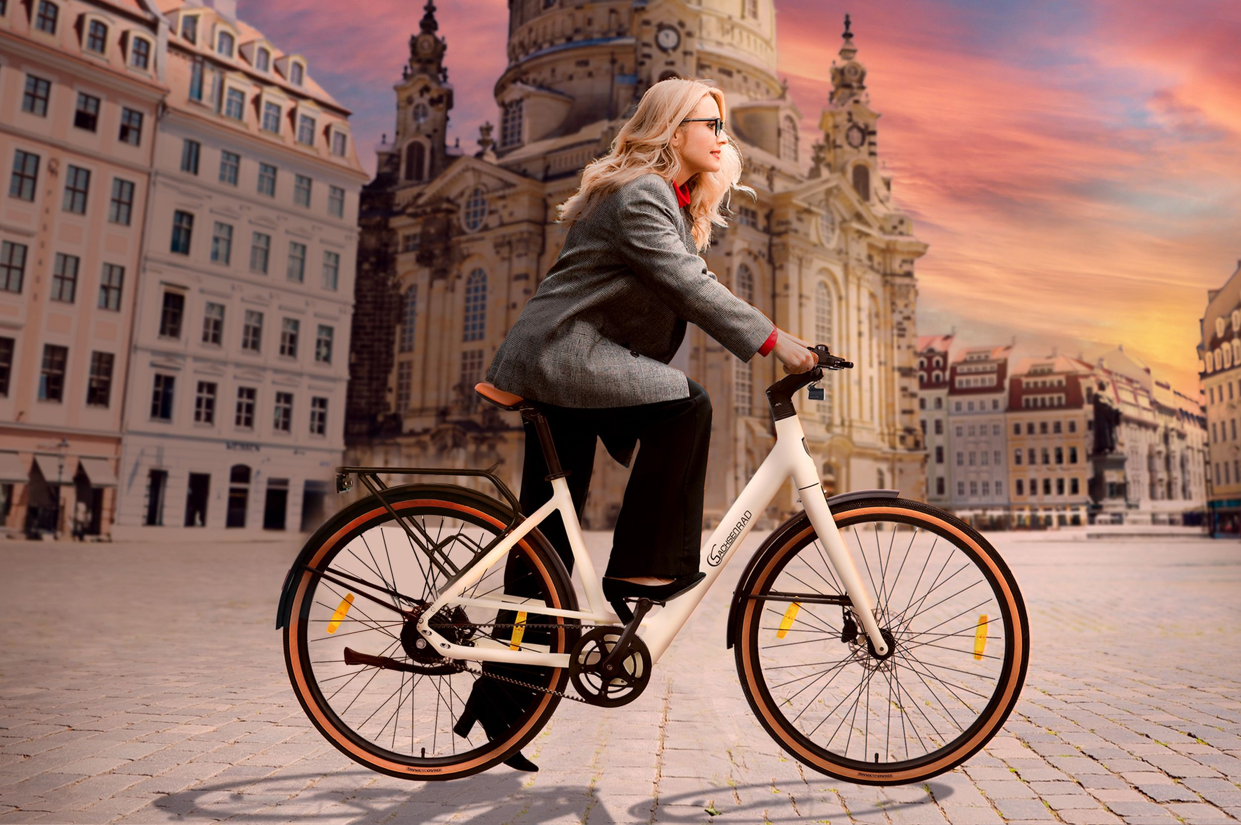 Eine Frau fährt mit einem weißen Fahrrad auf einer Straße in der Stadt. Gebäude im Hintergrund, Himmel ist bunt.
