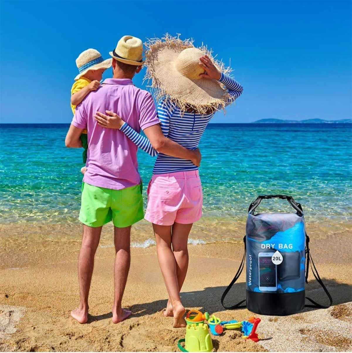 Eine Familie am Strand mit einem Trockenbeutel, einem Kind und Spielzeug. Das Wasser ist blau und der Himmel klar.