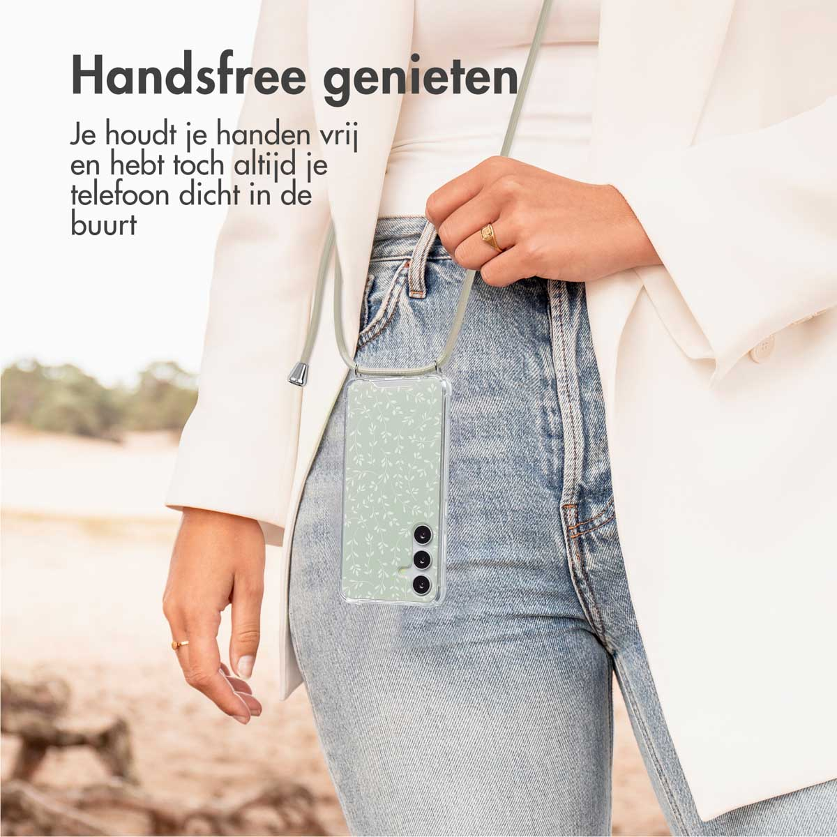 Une femme porte un blazer blanc et un jean bleu. Elle tient un téléphone avec une coque et un cordon.