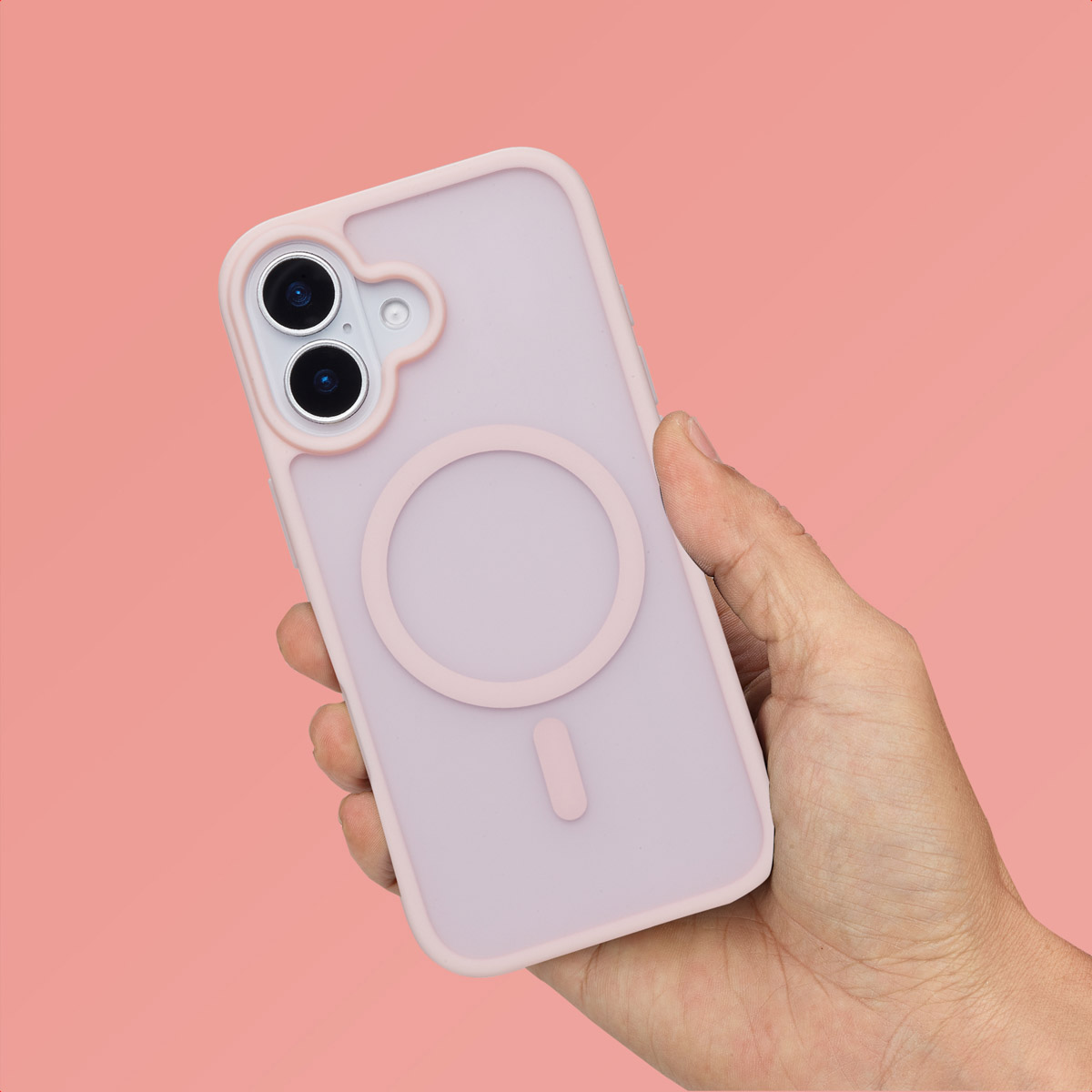 Hand die een lichtroze telefoonhoes vasthoudt met een roze ring en camera-uitsparing, op roze achtergrond.